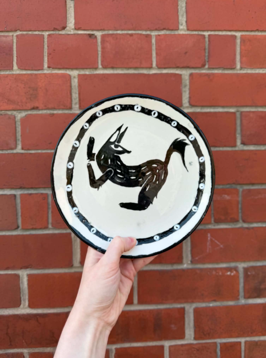 Hand holding a decorative plate with a black and white artistic image of a kangaroo in front of a brick wall.