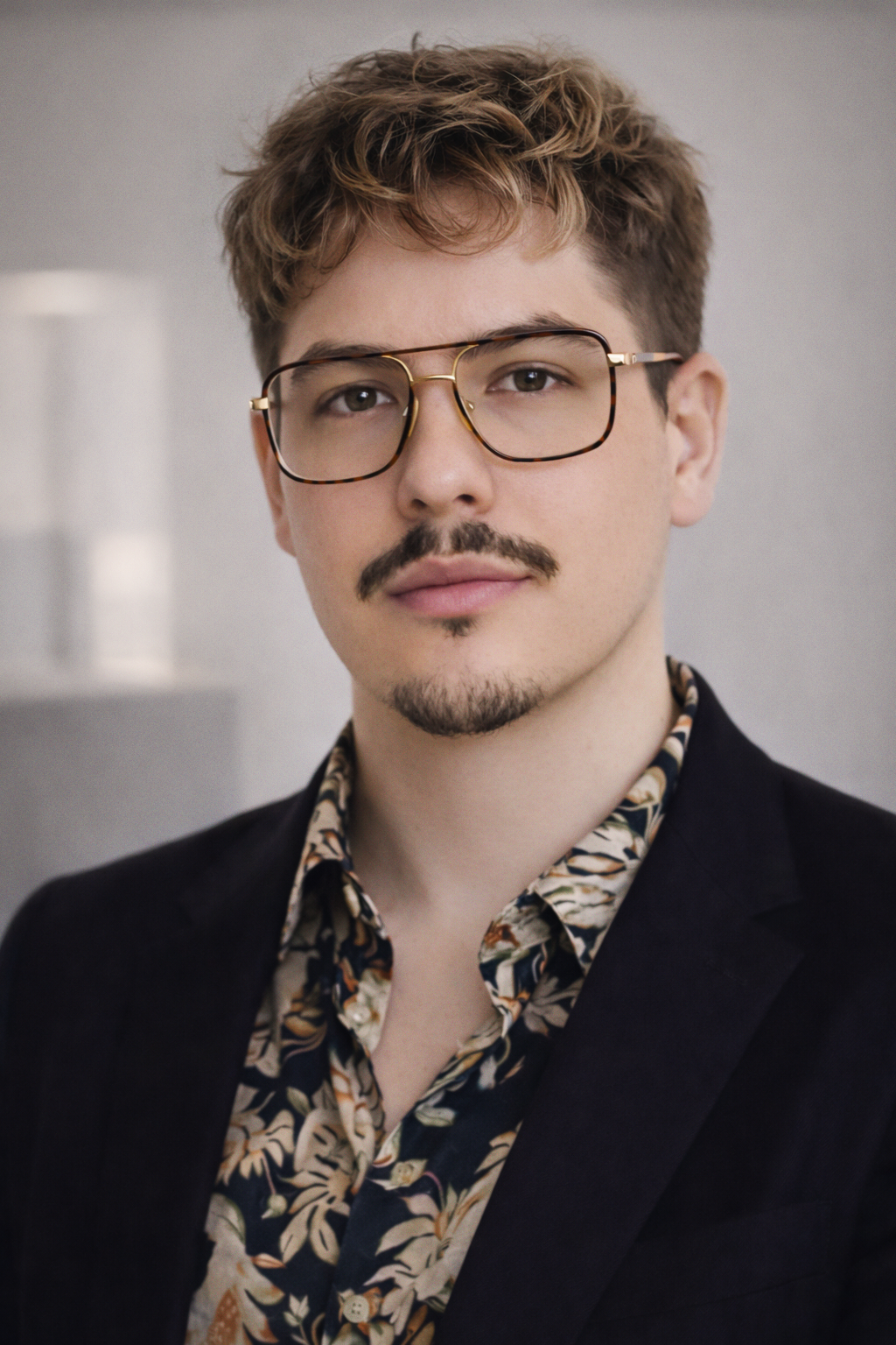 Portrait of Bojan Ristic, CMO of Stavrok, wearing glasses, a dark blazer, and a patterned shirt, looking at the camera with a confident and vibrant presence.