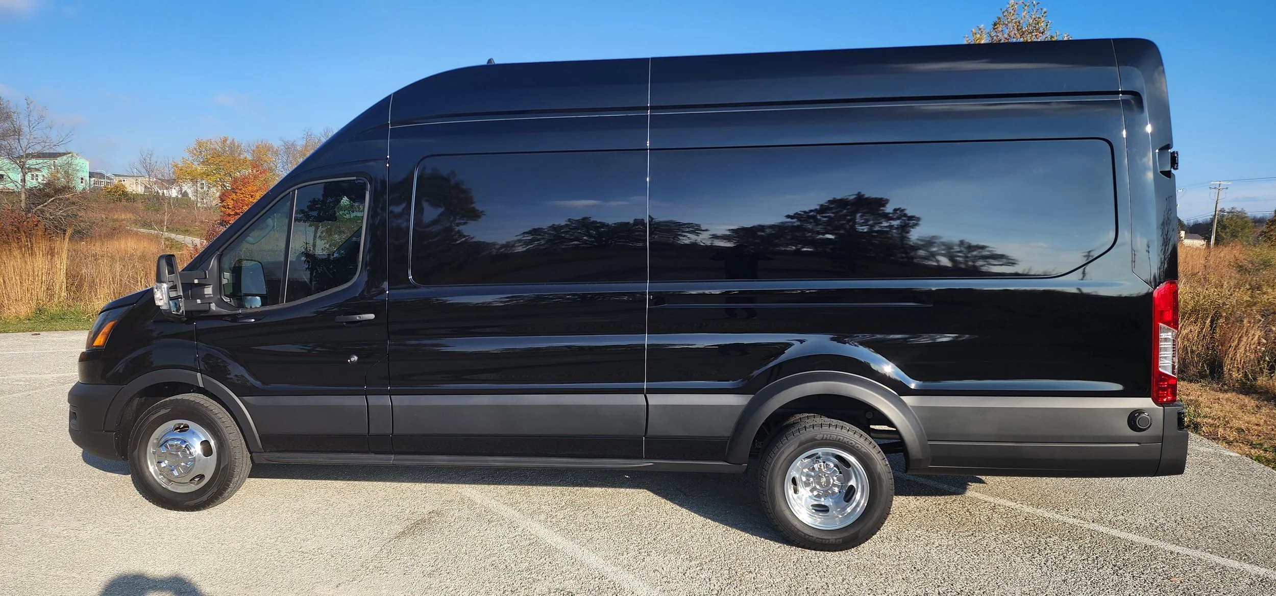 Black cargo van parked outdoors on a paved surface with trees and buildings in the background.