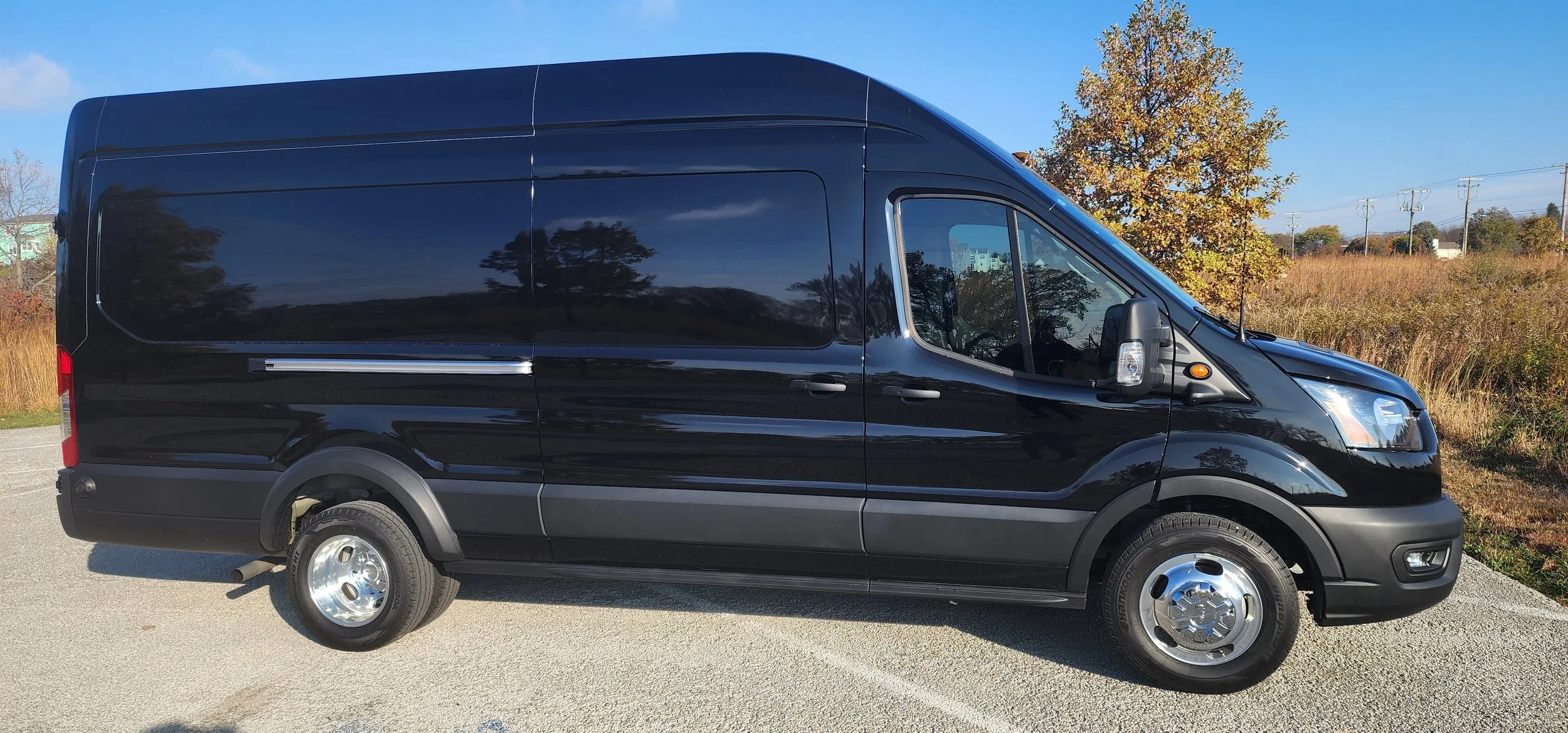 Black cargo van parked outdoors on a clear day with trees and a grassy field in the background.
