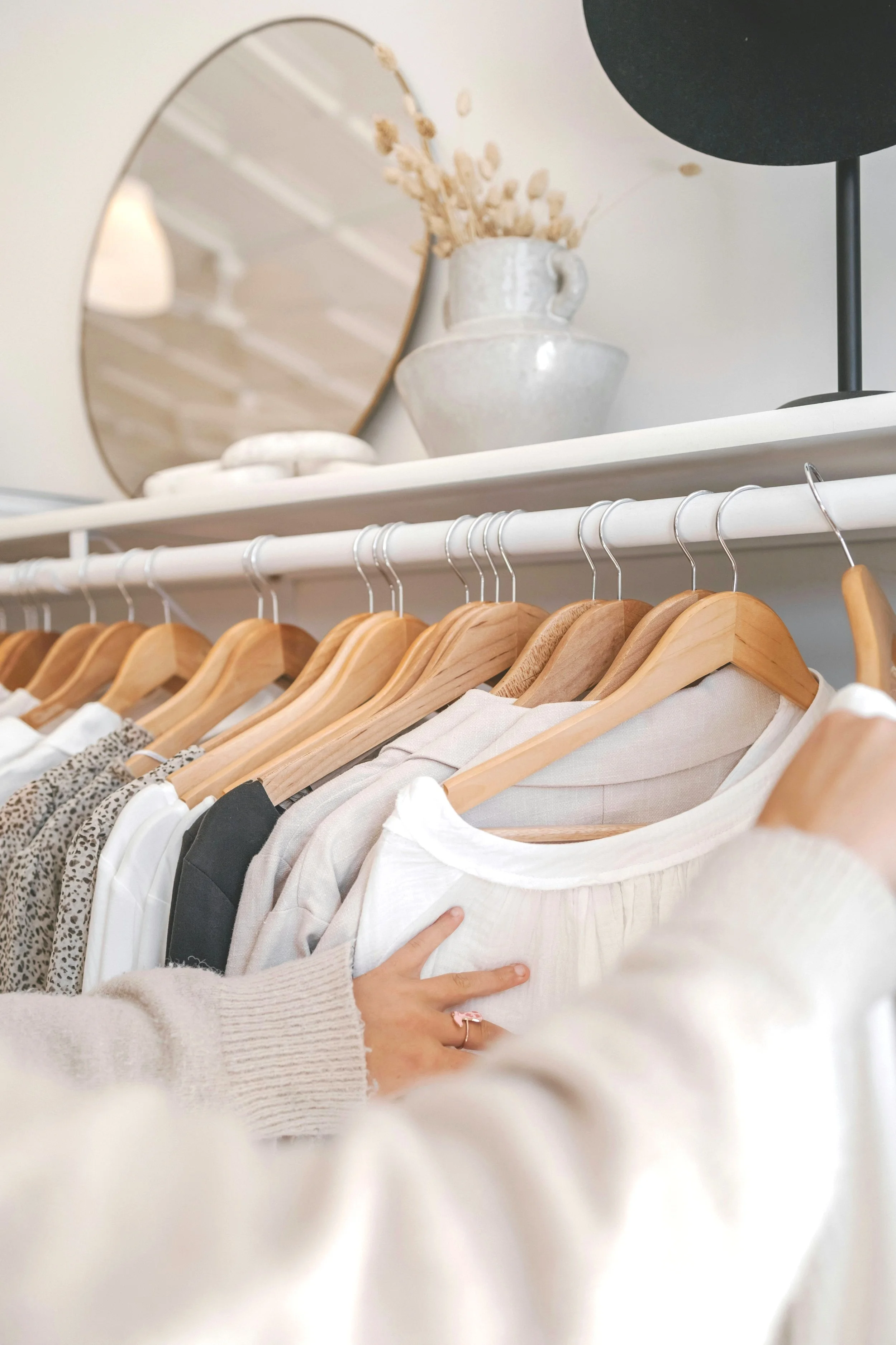 two hands organizing hanging clothes in a closet