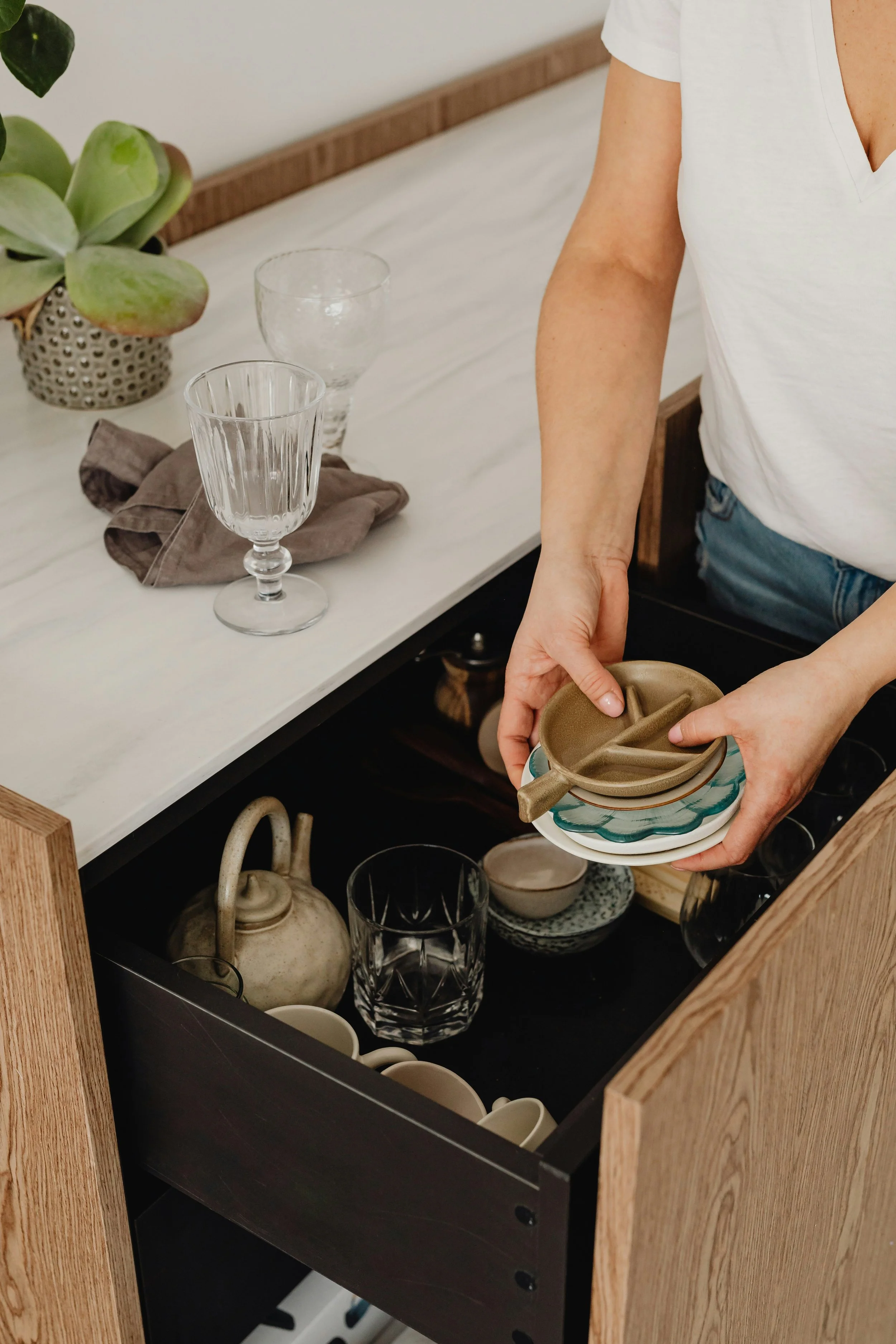 two hands placing dishes into a kitchen drawer