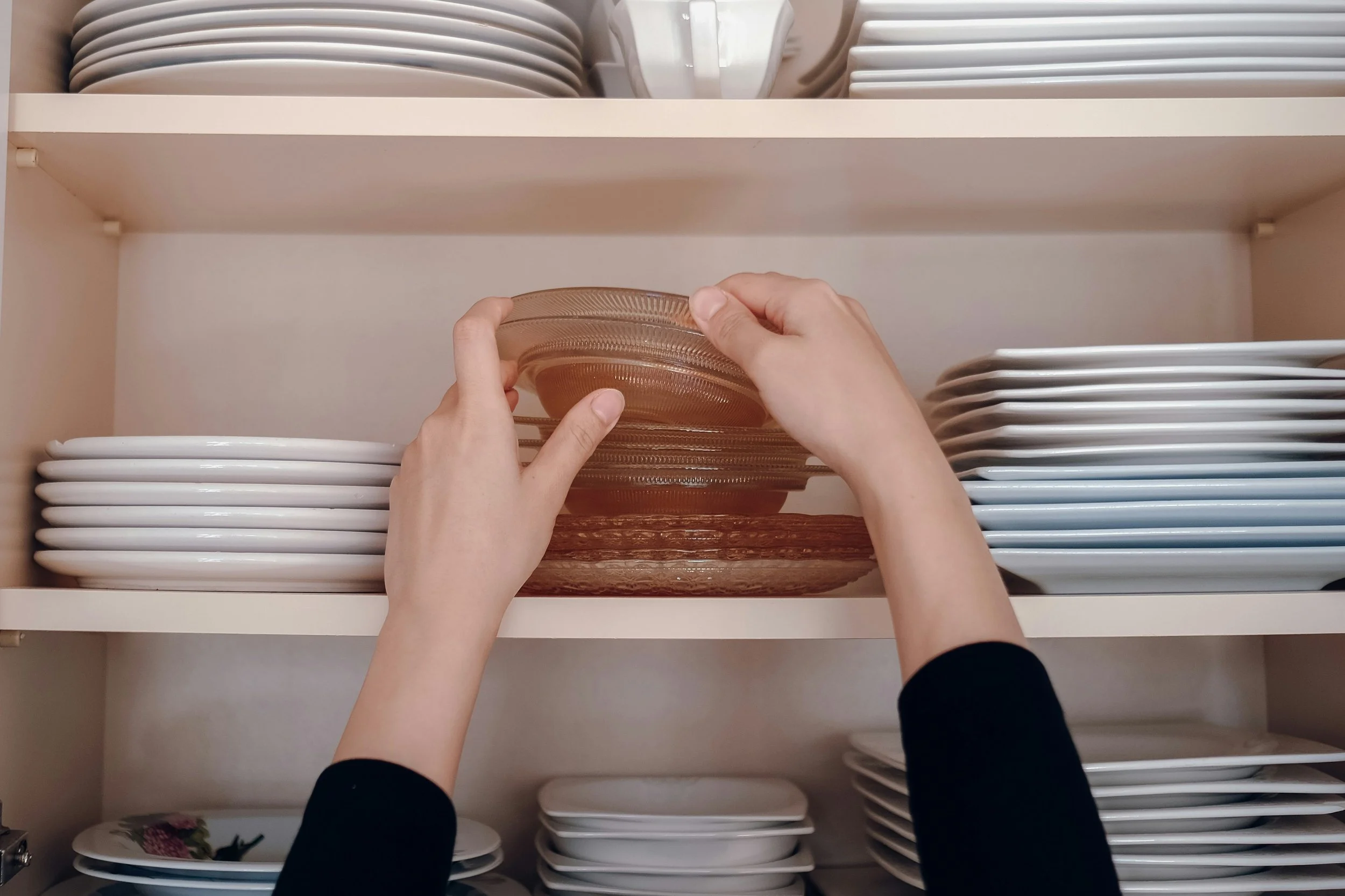 two hands organizing dishes into a cabinet