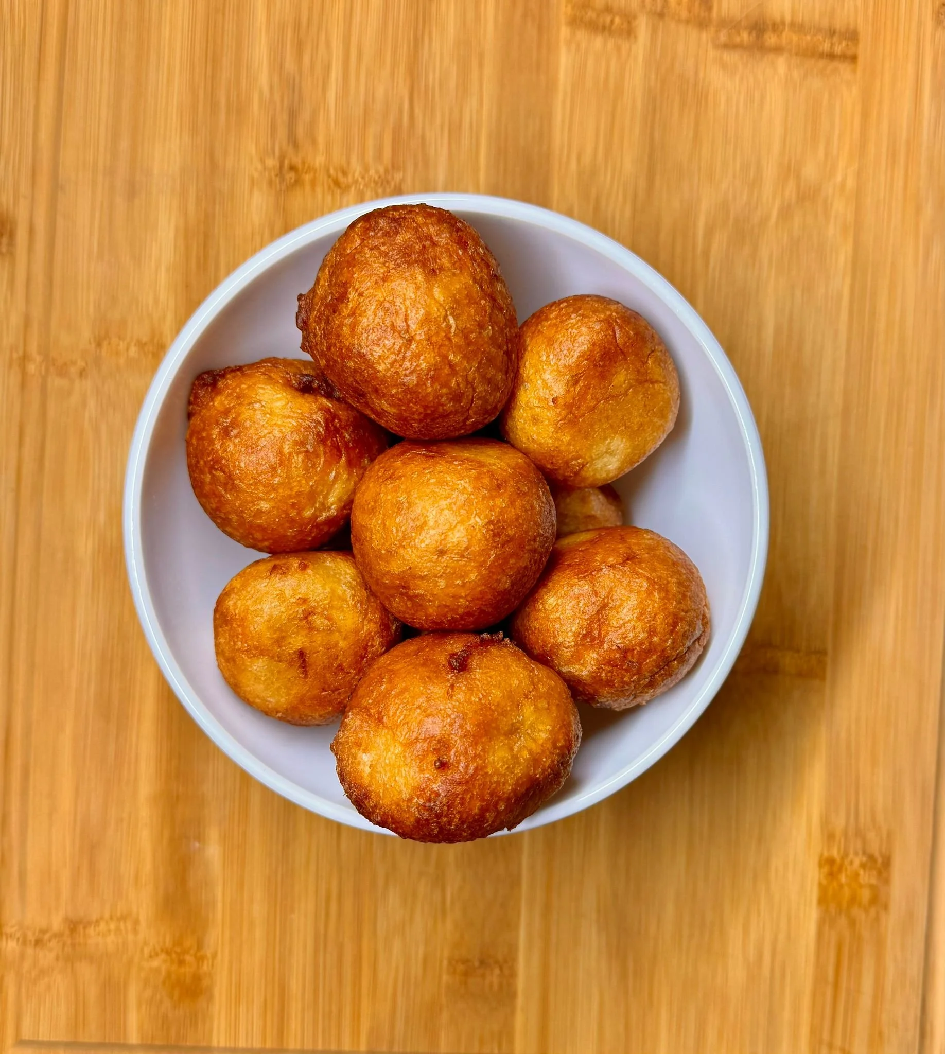 A white bowl filled with golden brown fried balls, placed on a wooden surface.