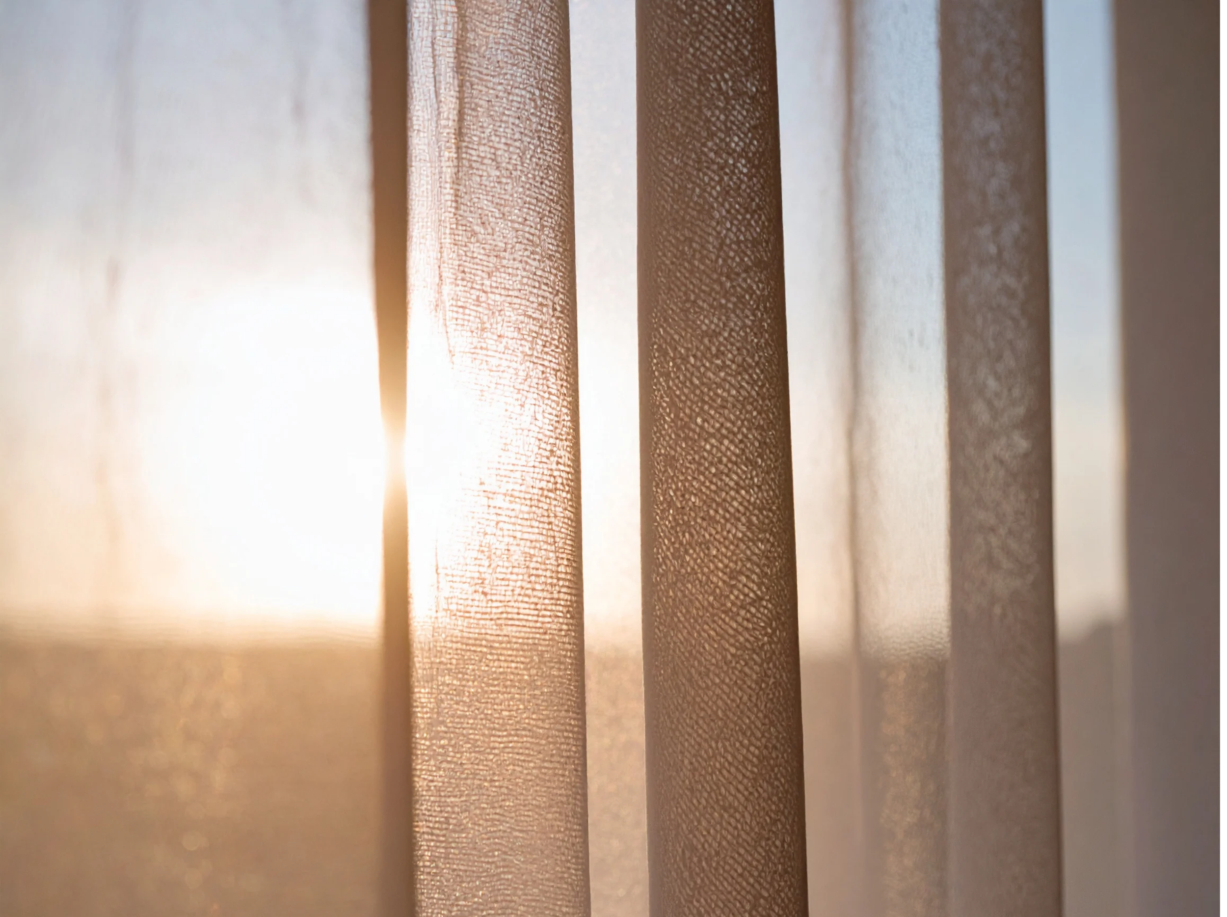 Close-up of vertical wooden blinds with sunlight shining through, highlighting the textured surface of the blinds.