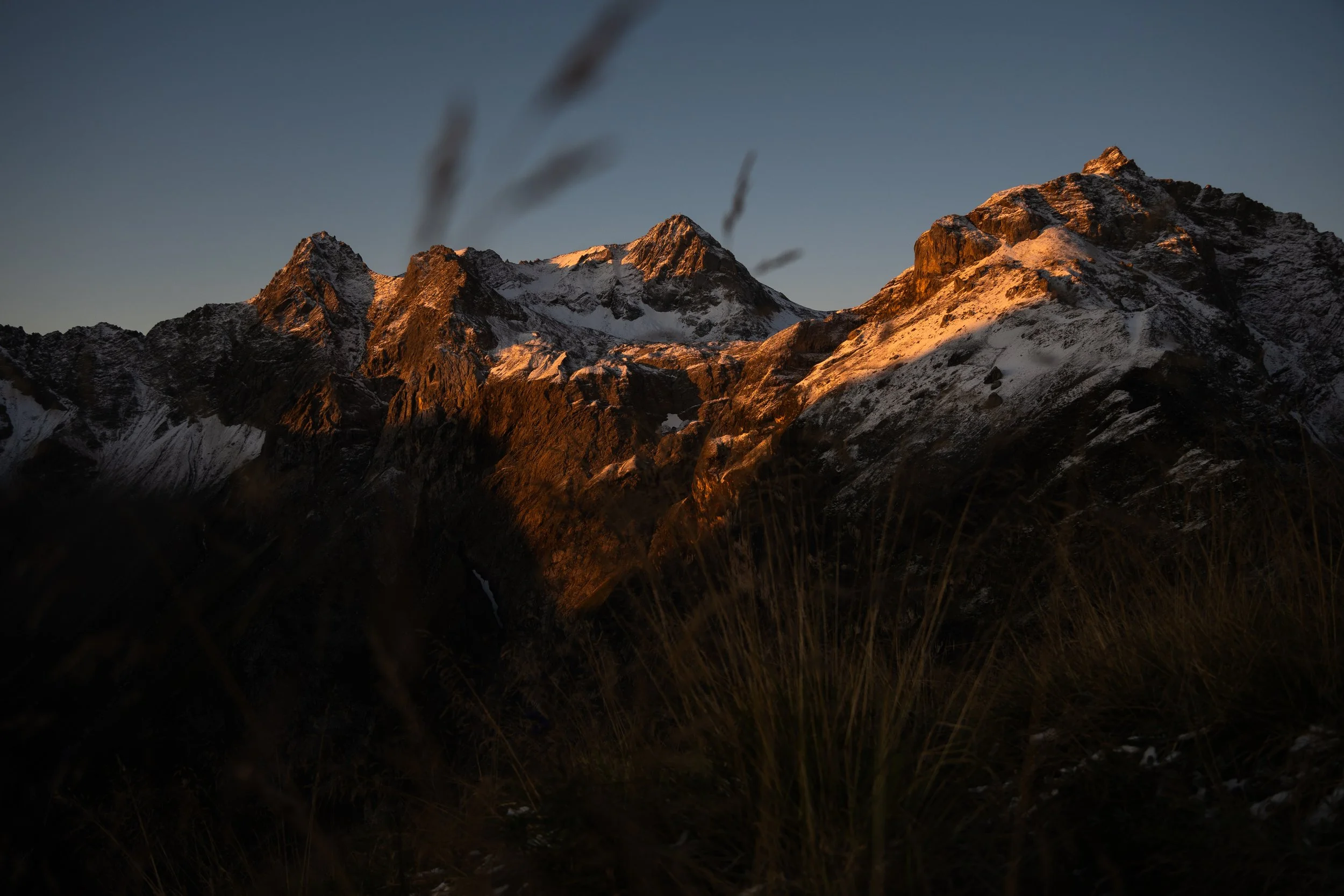Berggipfel bei Sonnenaufgang mit Schneebedeckten Gipfeln und dunklem Himmel.
