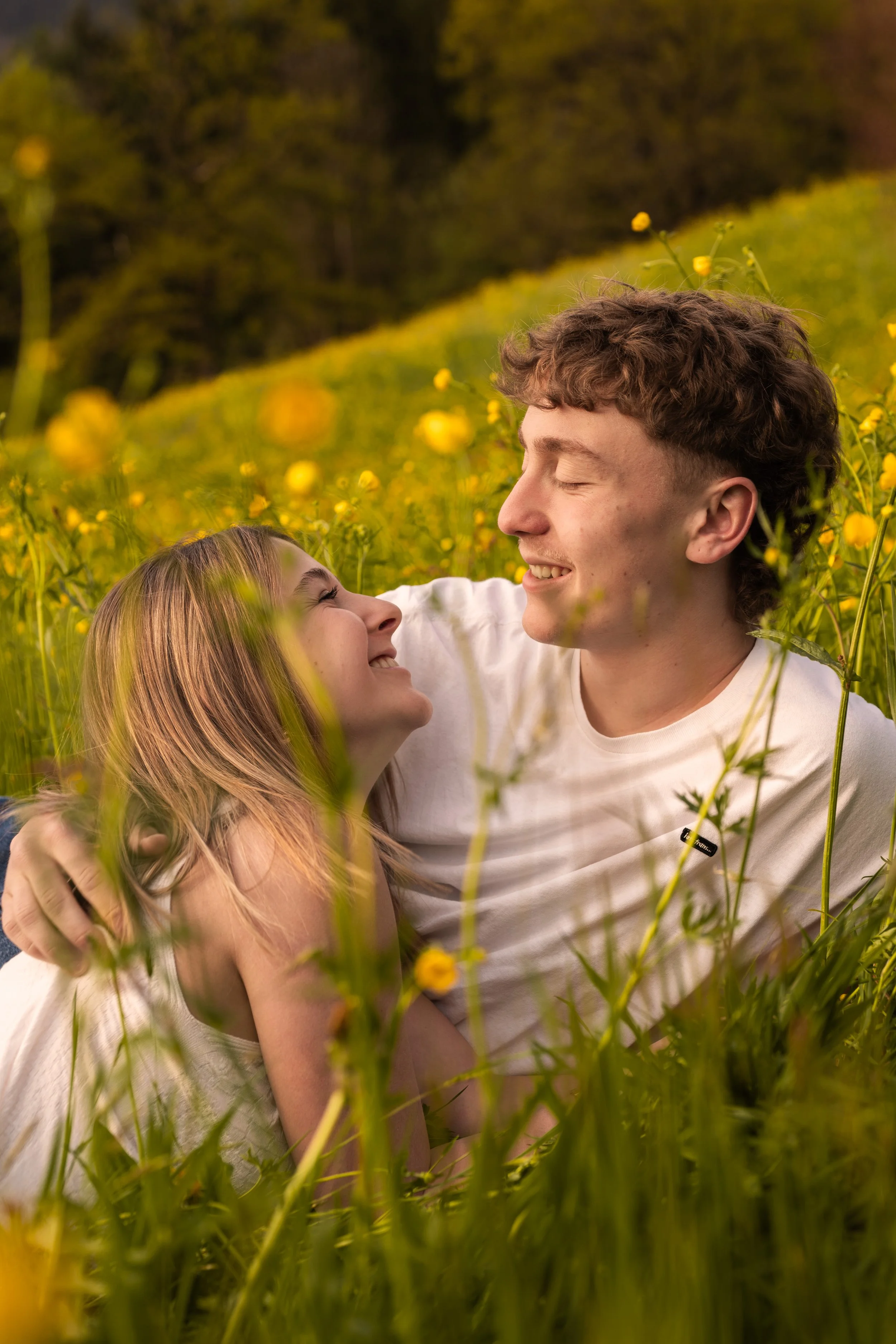 Ein Paar lieg auf einer blühenden Wiese. Die Blicke treffen sich, umgeben von gelben Blumen.