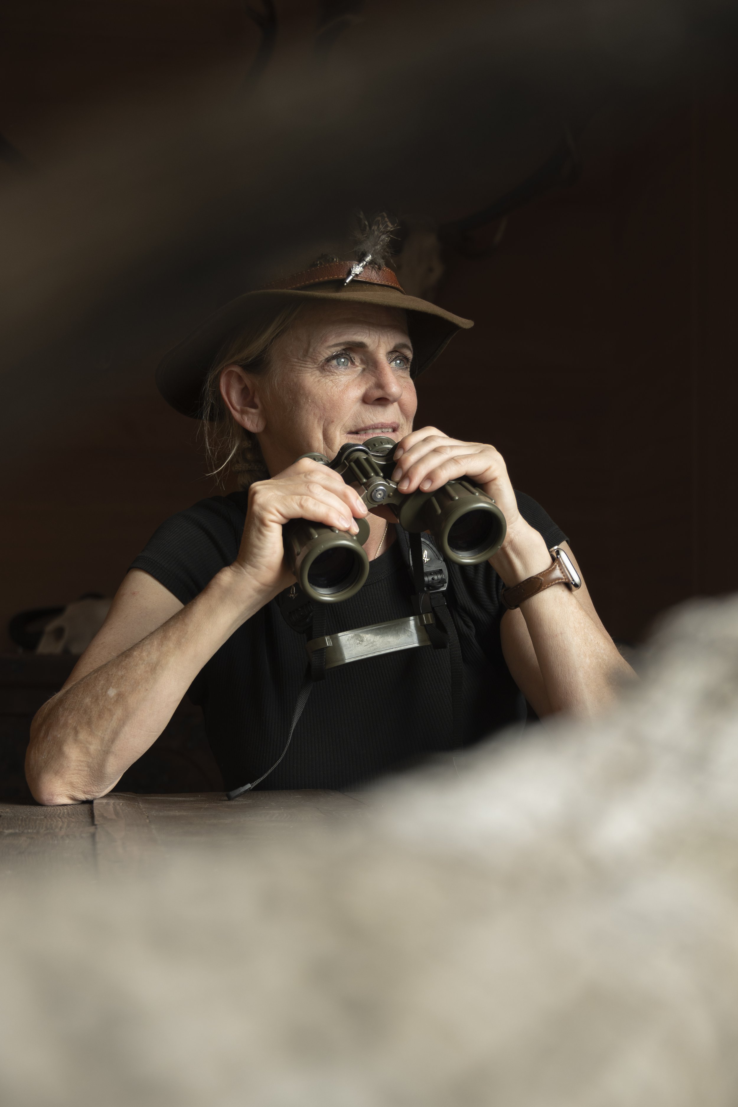 Frau mit Jagdhut schaut durchs Fernglas.