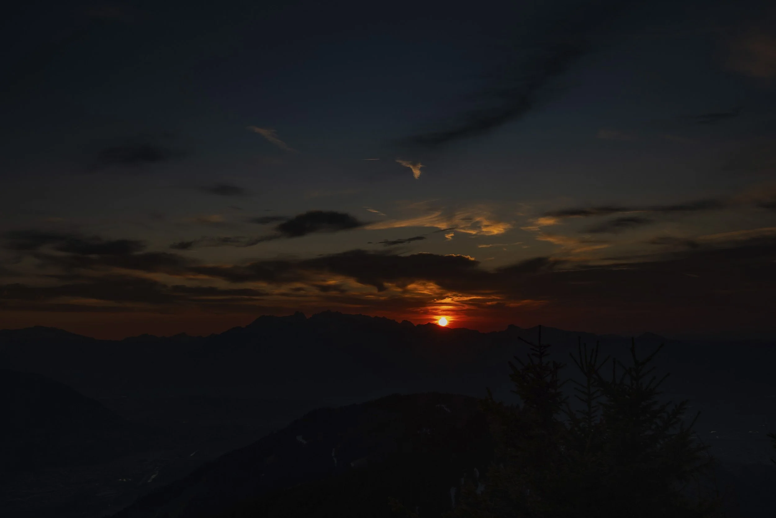 Ein Sonnenuntergang hinter Bergen mit Wolken am Himmel.