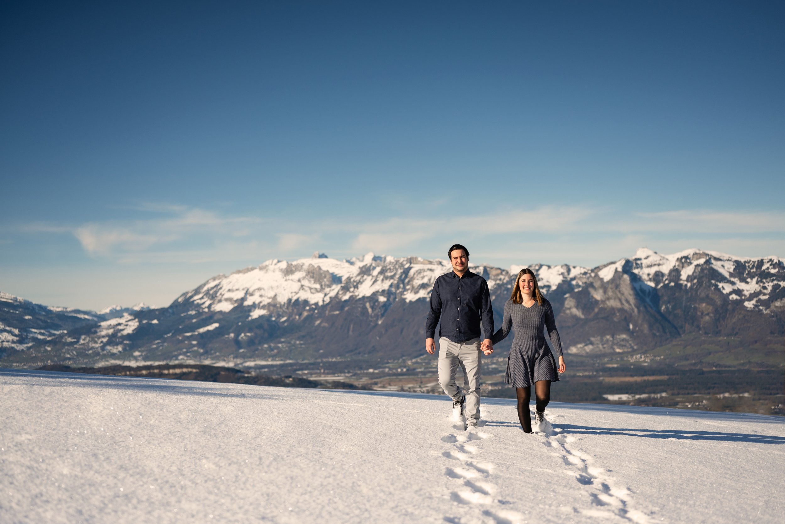 In einer wunderschönen Winterlandschaft läuft ein Paar händehaltend durch den Schnee.
