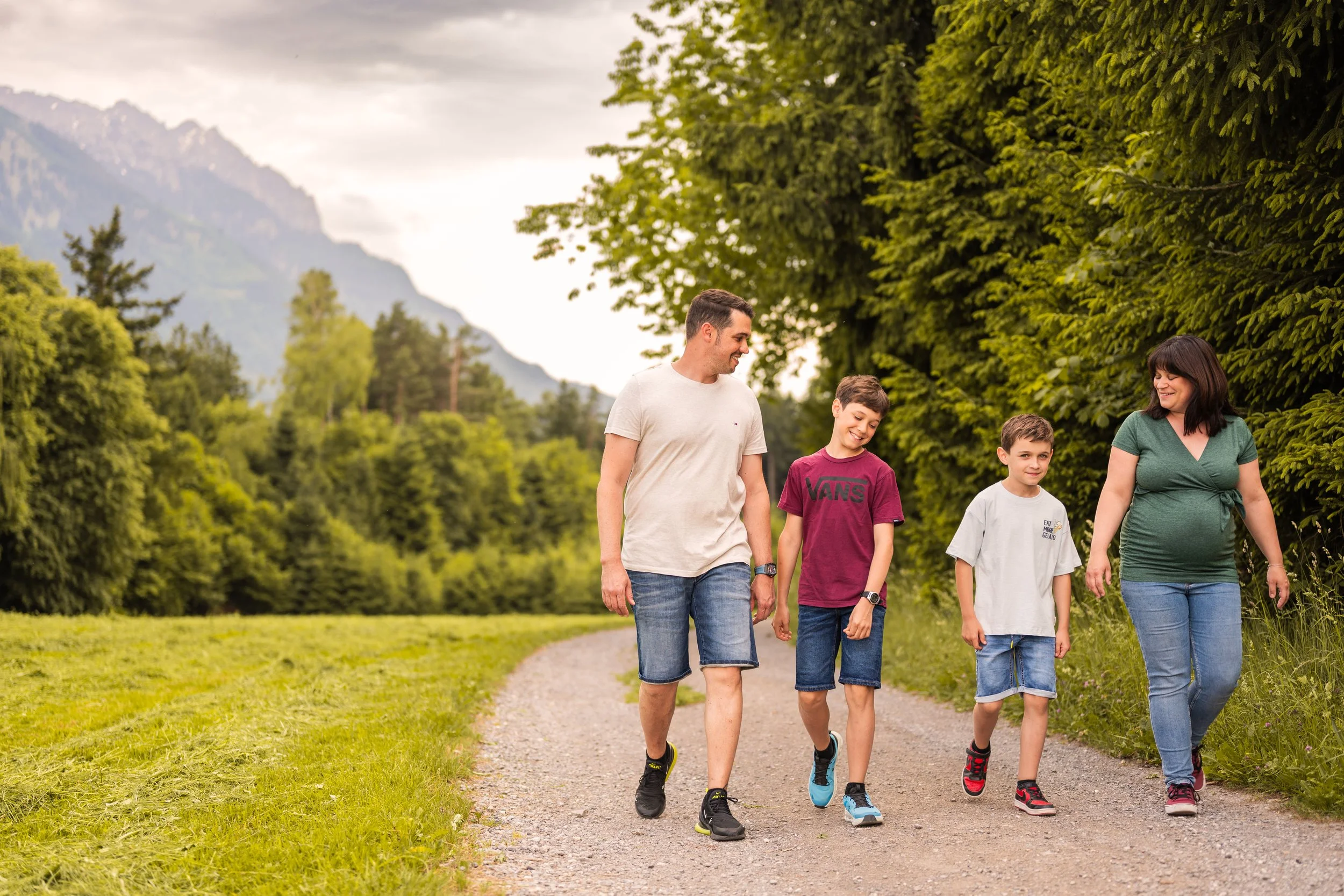 Eine Familie läuft zusammen einen Weg entlang. Links der Papa, rechts die schwangere Mama und in der Mitte die beiden Söhne.