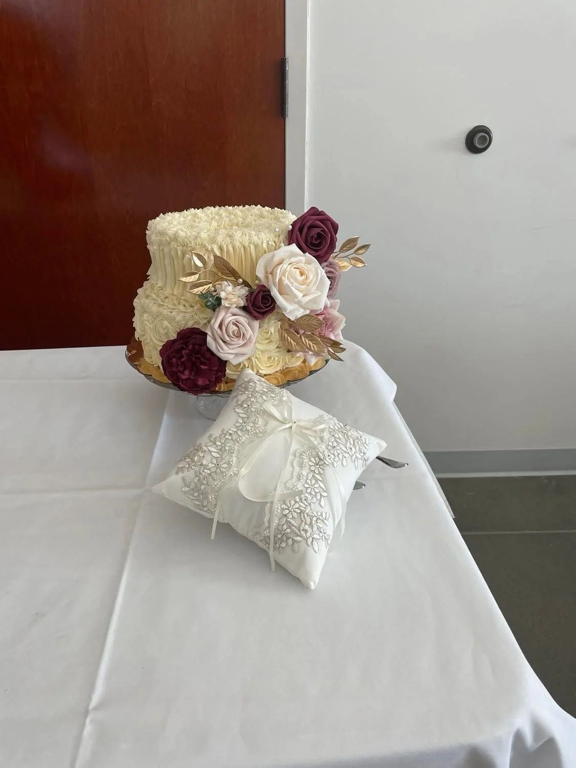 A wedding cake decorated with flowers and a white embroidered pillow.