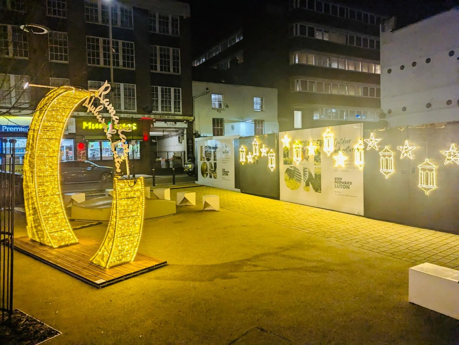 Nighttime city scene with illuminated yellow arch and decorative hanging lanterns and stars against a building backdrop.