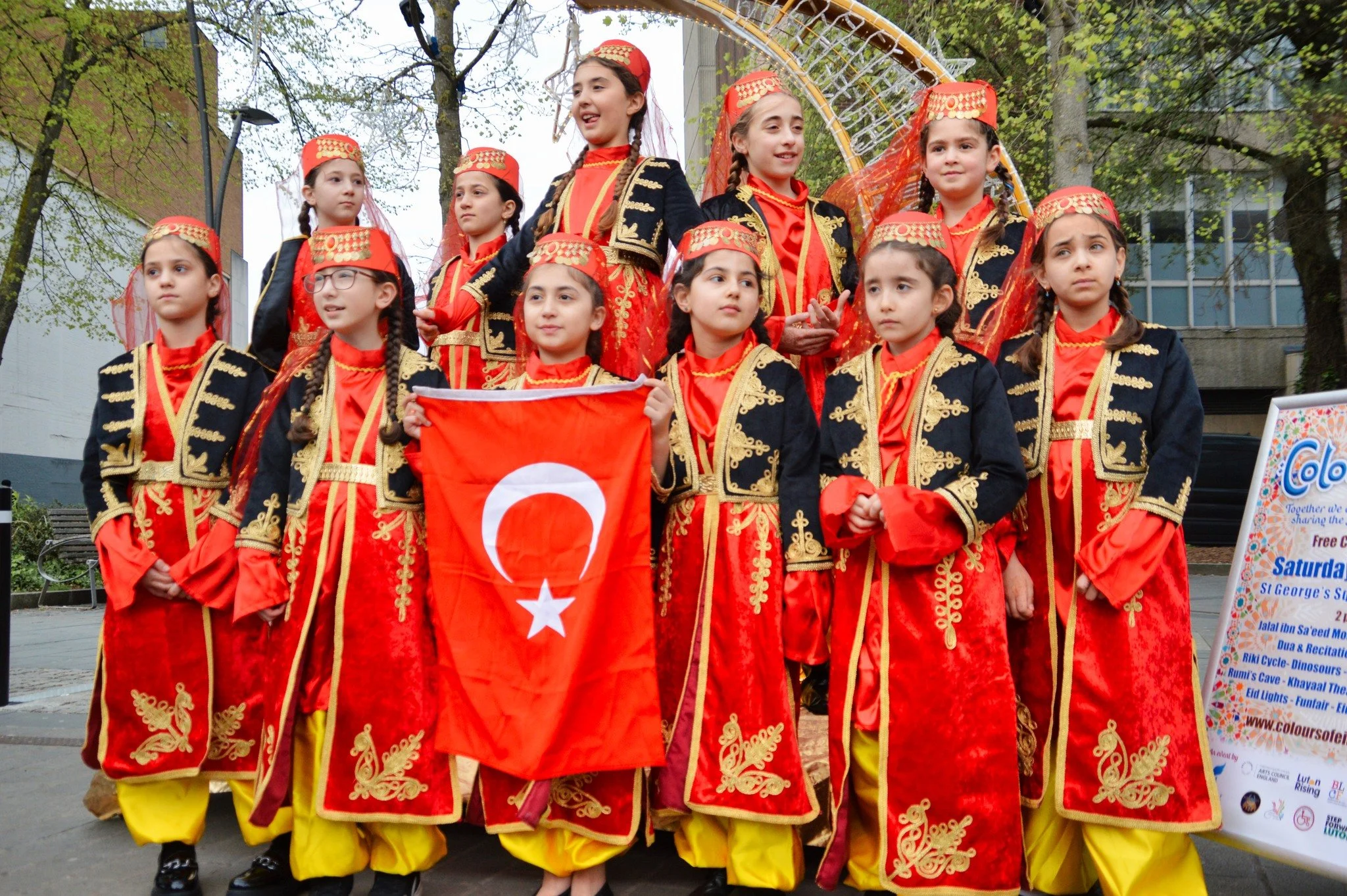 Group of young girls in traditional Turkish costumes holding a Turkish flag during a cultural event or celebration.