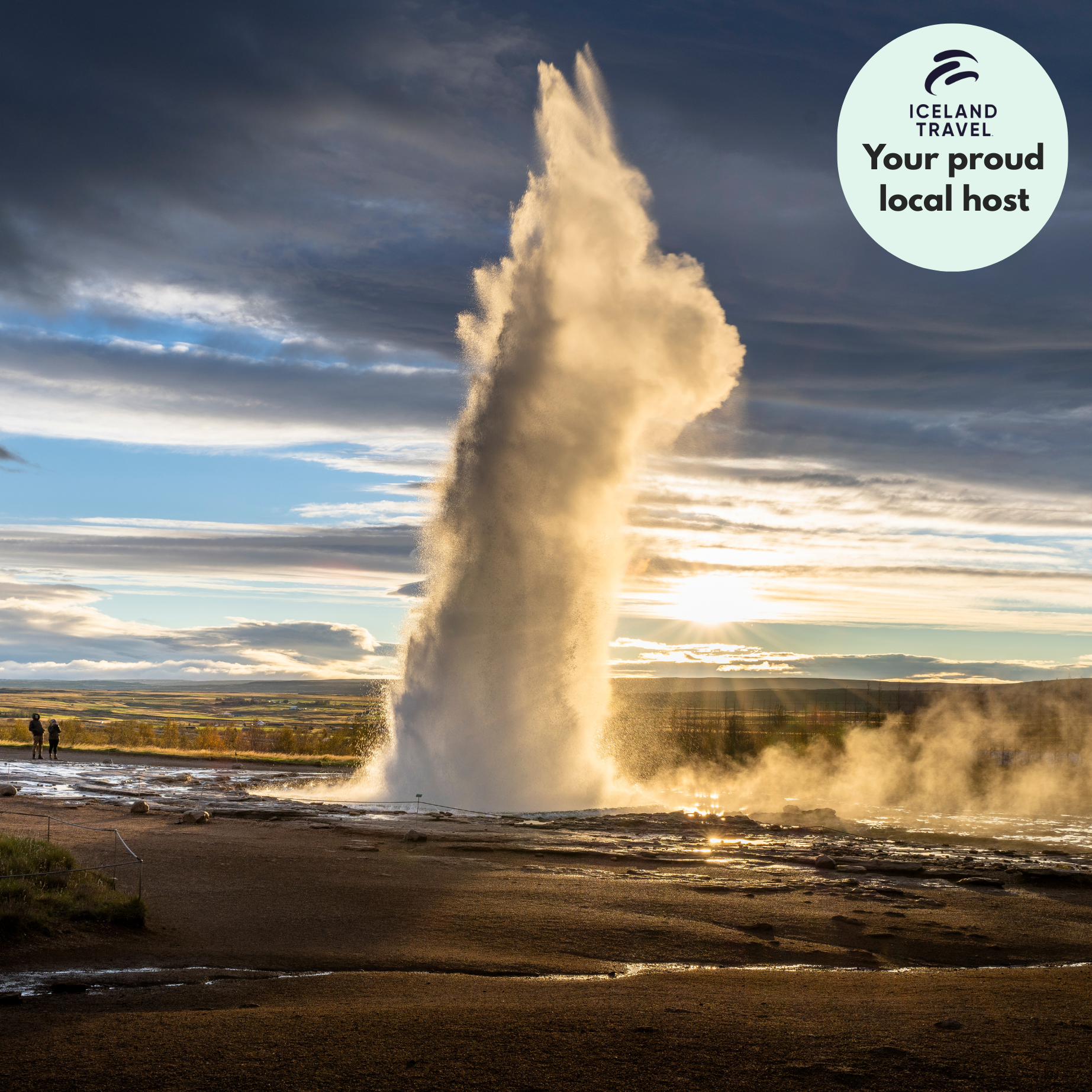 A geyser erupting with a tall water column in a landscape during sunset, with clouds and two people observing in the distance.