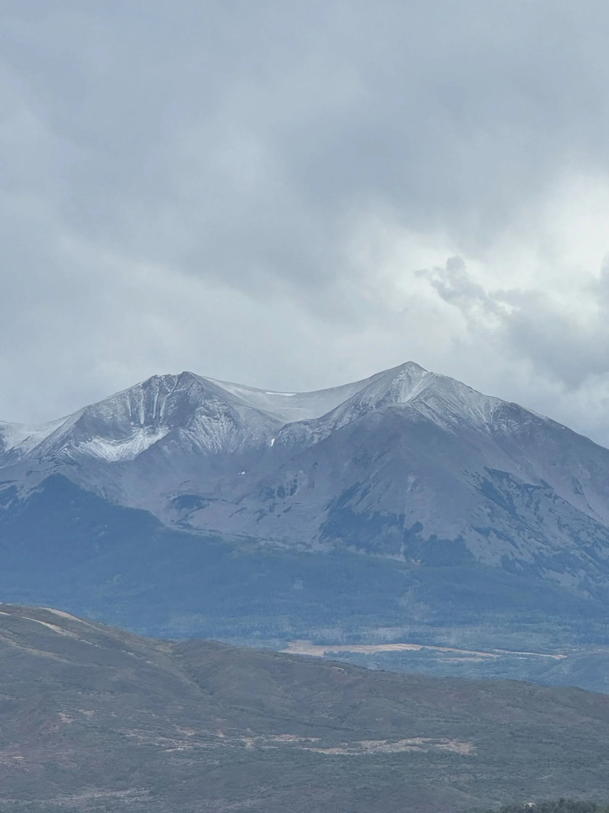Mountain range with snow-capped peaks under cloudy sky in a natural landscape.