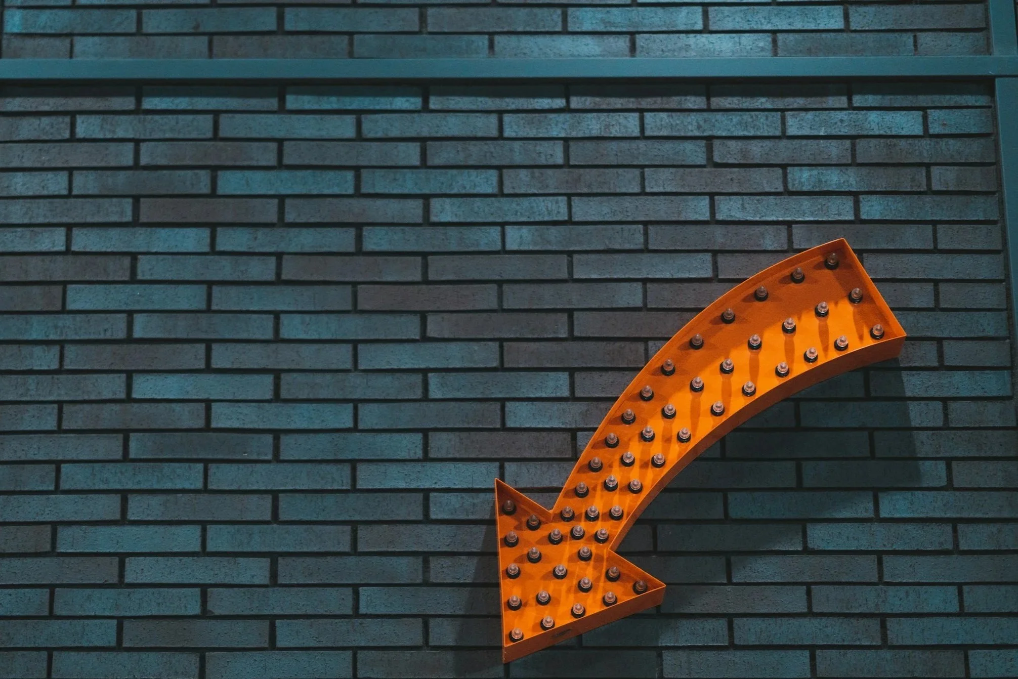 Orange arrow-shaped marquee light sign mounted on a dark brick wall.