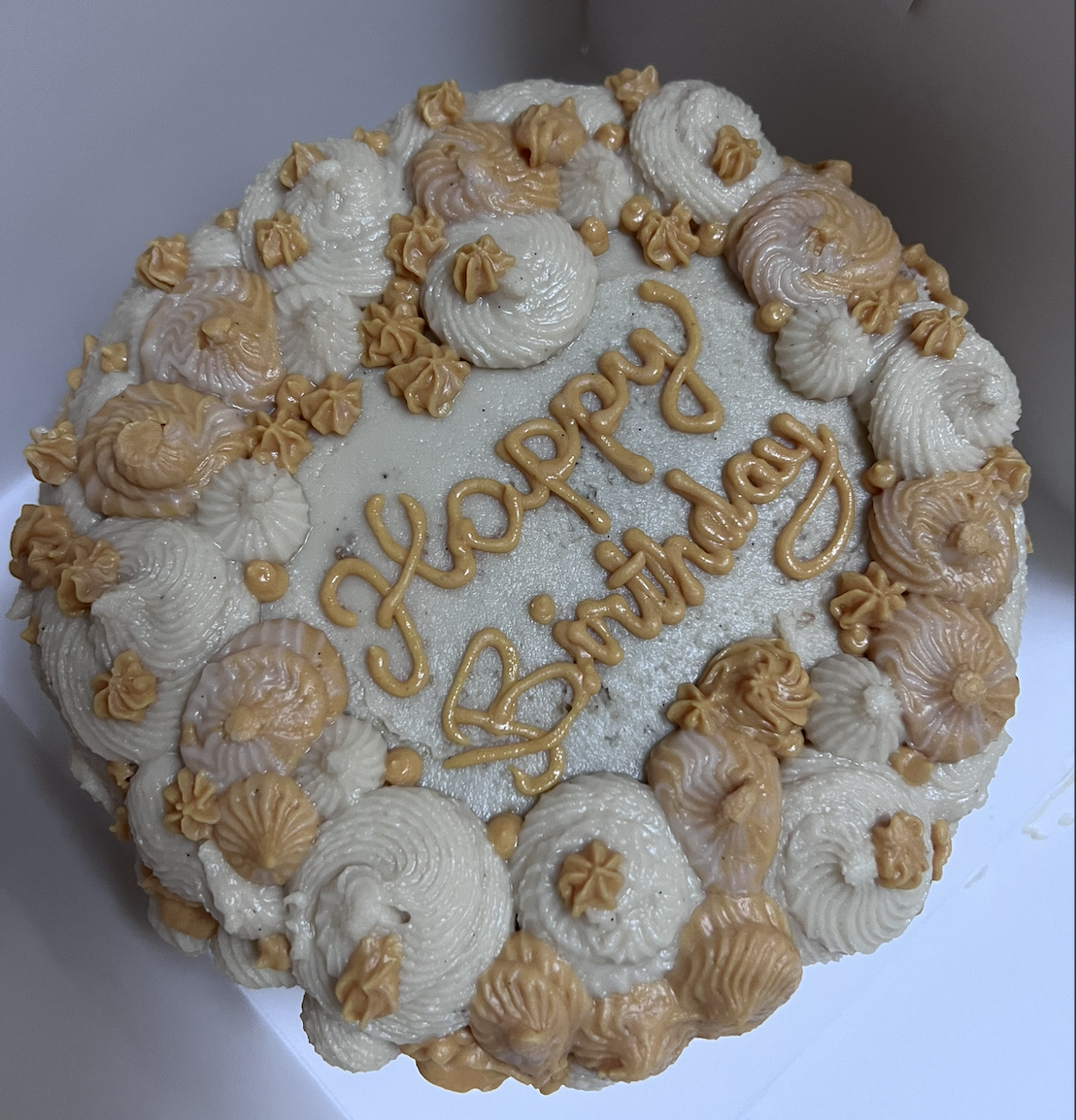 A birthday cake decorated with white and light brown frosting, with the message 'Happy Birthday' written on top.