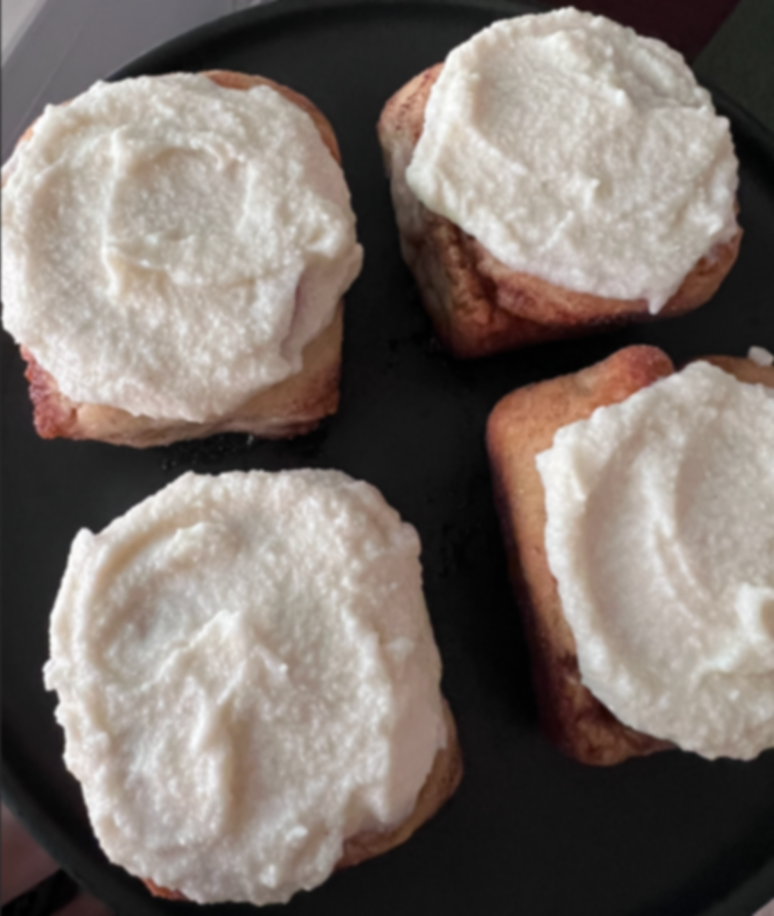 Four pieces of toast with a generous spread of butter on top, on a black plate.