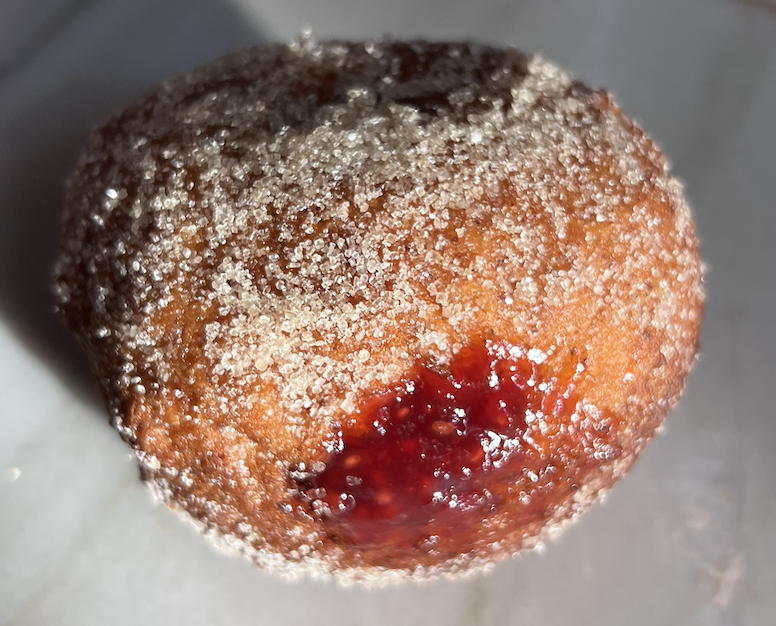 Close-up of a fried donut with powdered sugar and a jam filling
