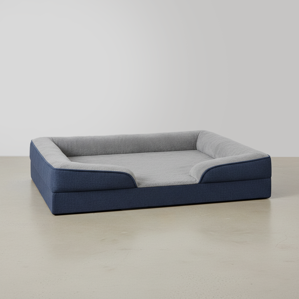 A rectangular pet bed with a cushioned interior and raised sides, featuring a color block design with gray inside and navy blue outside, placed on a light wood floor against a plain white wall.