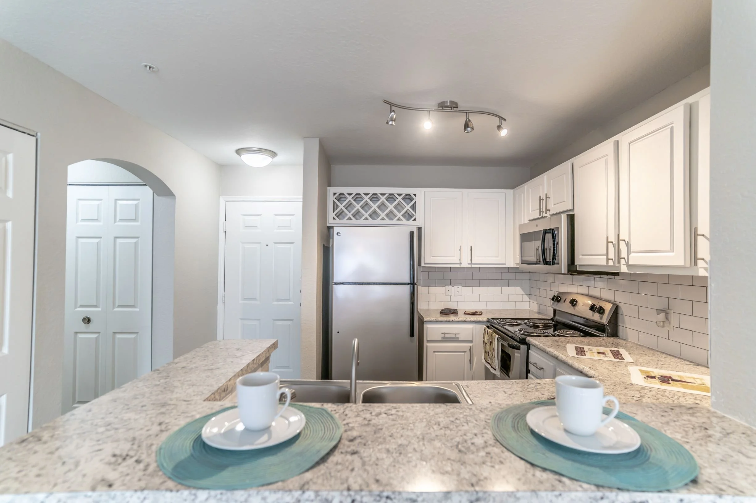 Kitchen with granite countertops, white cabinets, stainless steel refrigerator, microwave, and stove. Two cups on placemats on the counter.