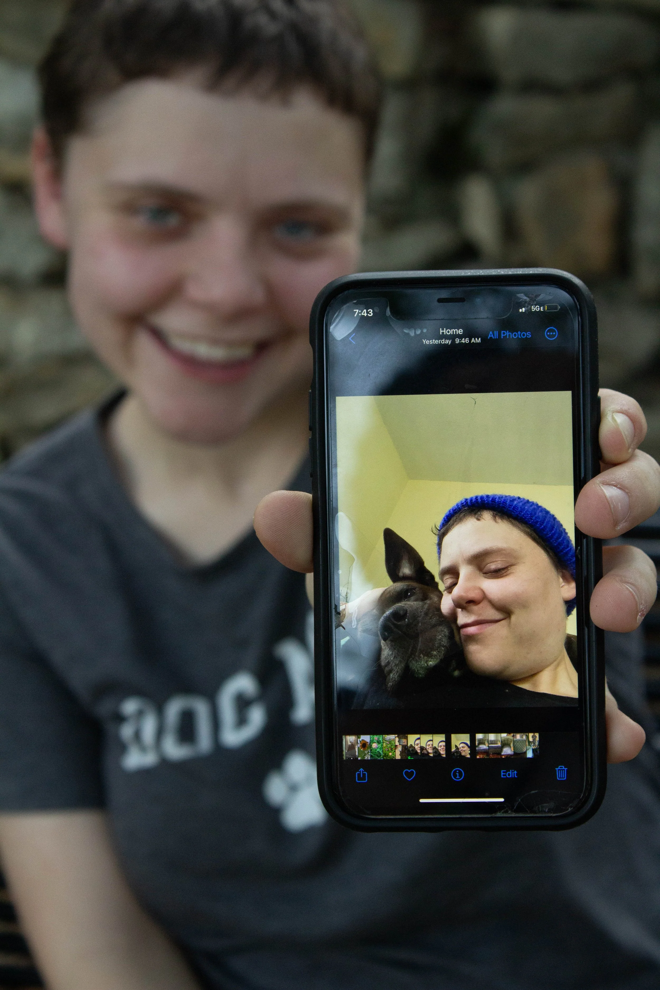 Person holding a smartphone showing a photo of themselves and a dog, both with eyes closed, cuddling.