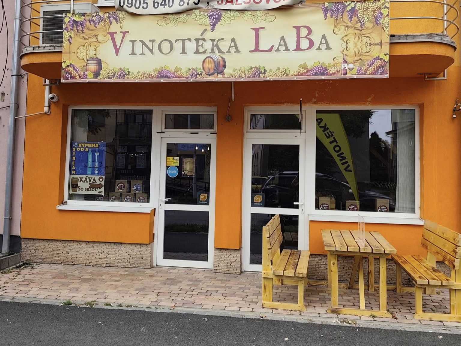 Exteriér budovy s nápisom „VINOTÉKA“ nad vchodom. Budova má bielu fasádu, čierny vchod a červenú škridlovú strechu s čiernym odkvapom.