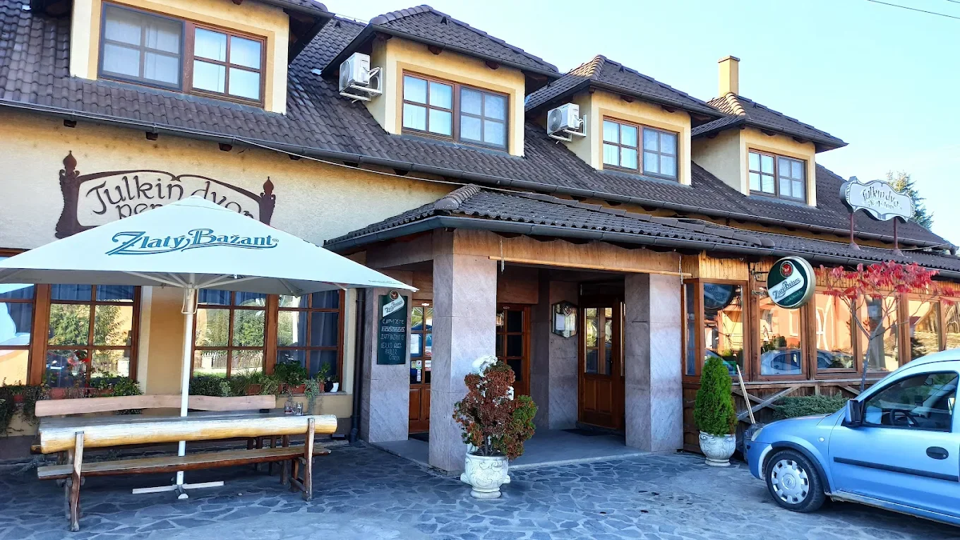 Exteriér reštaurácie s veľkým slnečníkom a drevenými lavicami vonku, oknami, nápis „Julkin dvor“ a „Zlaty Bazant“.