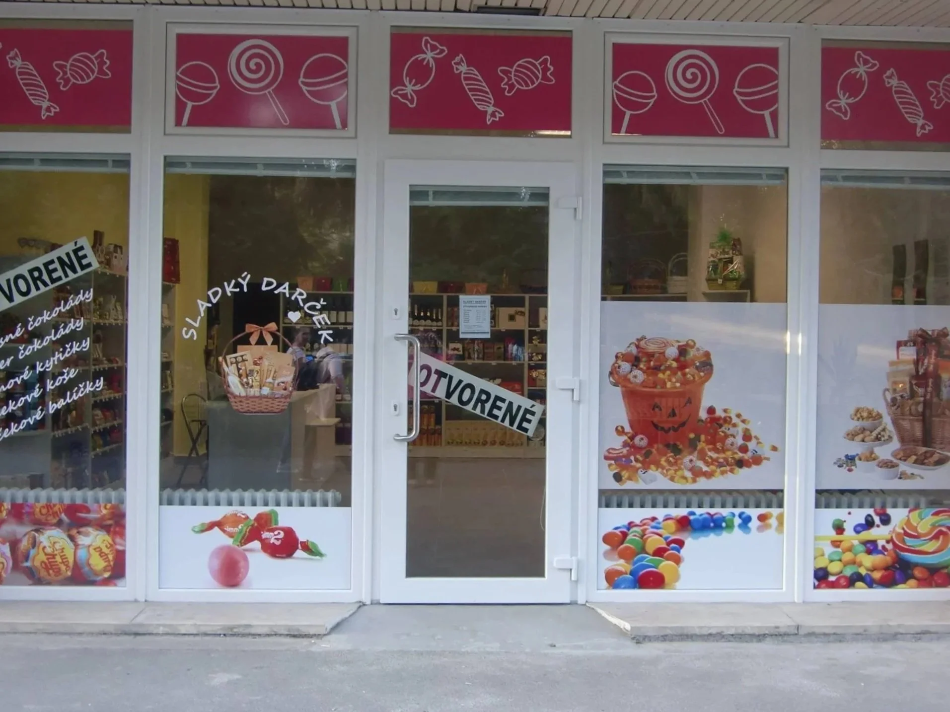 Výklad cukrárne s ružovými nápismi s lízankami a cukrovinkami, zdobený obrázkami rôznych cukrovín.