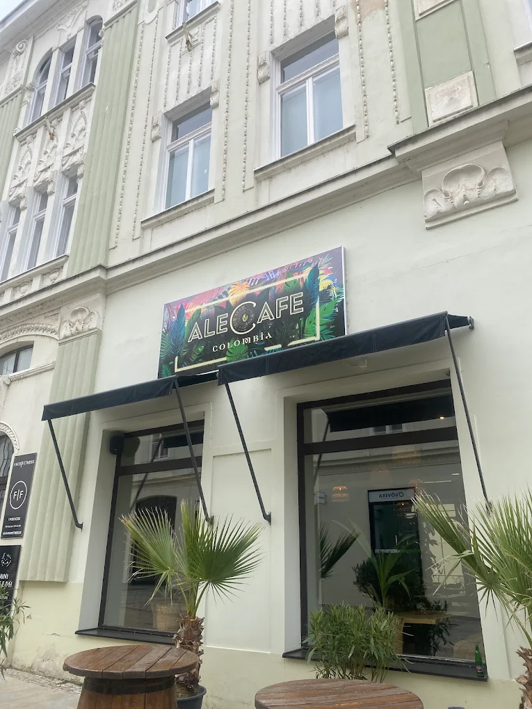 Exteriér kaviarne Ale Café v Nitre s farebným nápisom, čiernymi markízami nad oknami a palmami vonku.