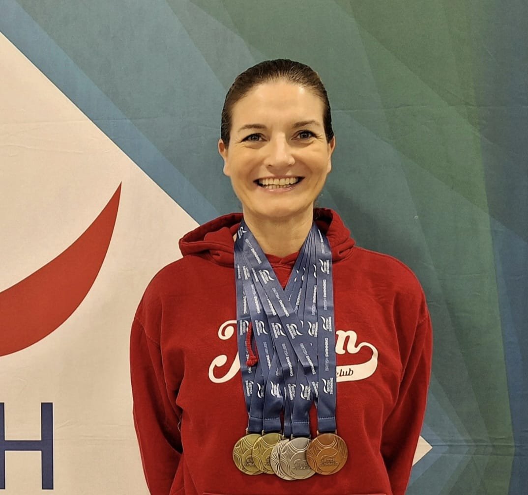 A woman wearing a red hoodie with medals around her neck, standing in front of a colorful background at a sporting event.