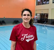 Woman standing by indoor swimming pool, wearing a red Trojan shirt.