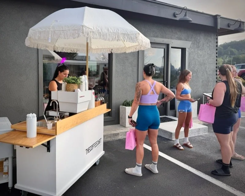 Group of women in athletic wear standing outside a coffee stand under a white umbrella.