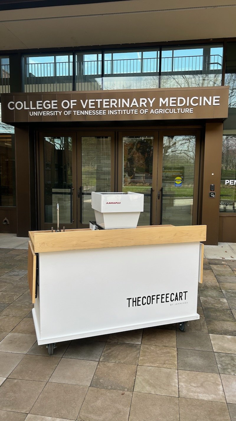 A white mobile coffee bar with the words 'THECOFFEE CART by Jennings' sits outside the College of Veterinary Medicine at the University of Tennessee Institute of Agriculture.