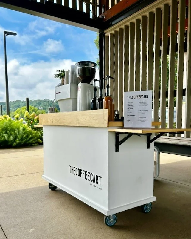 A mobile coffee cart with coffee brewing equipment and a menu sign outside a building, with a scenic outdoor view in the background catering a wedding shower in Knoxville.