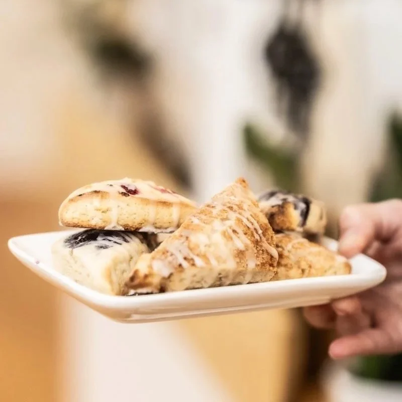 A person holding a white plate with various slices of pie, including blueberry, apple cinnamon, and possibly peach or banana.