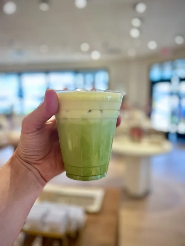 A hand holding a clear plastic cup with a green matcha latte inside, at a Kendra Scott Jewelry brand activation in Sevierville, Tennessee.