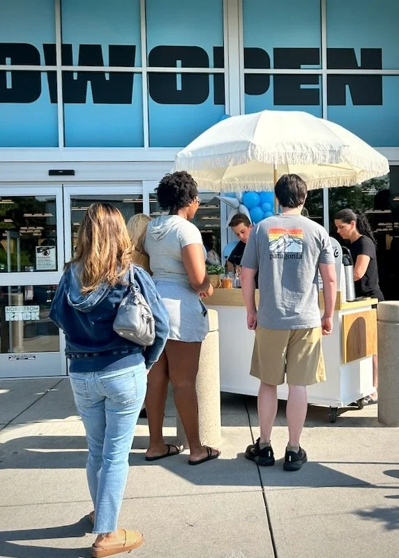 People standing in line at an outdoor vendor stand with a white umbrella in front of a popular coffee cart catering for a brand activation in Knoxville.