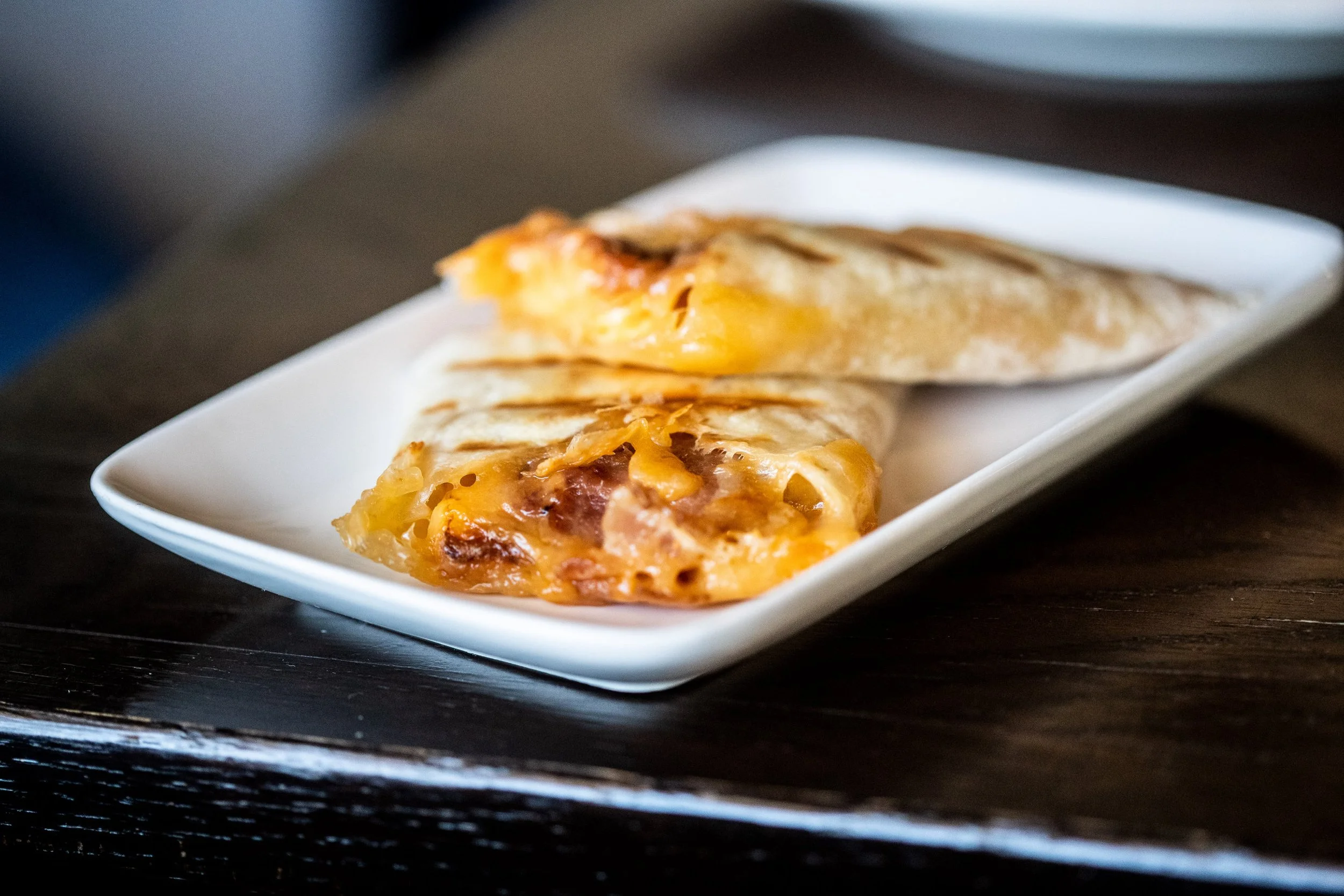 Two cheese-filled quesadillas on a white rectangular plate placed on a dark wooden table.