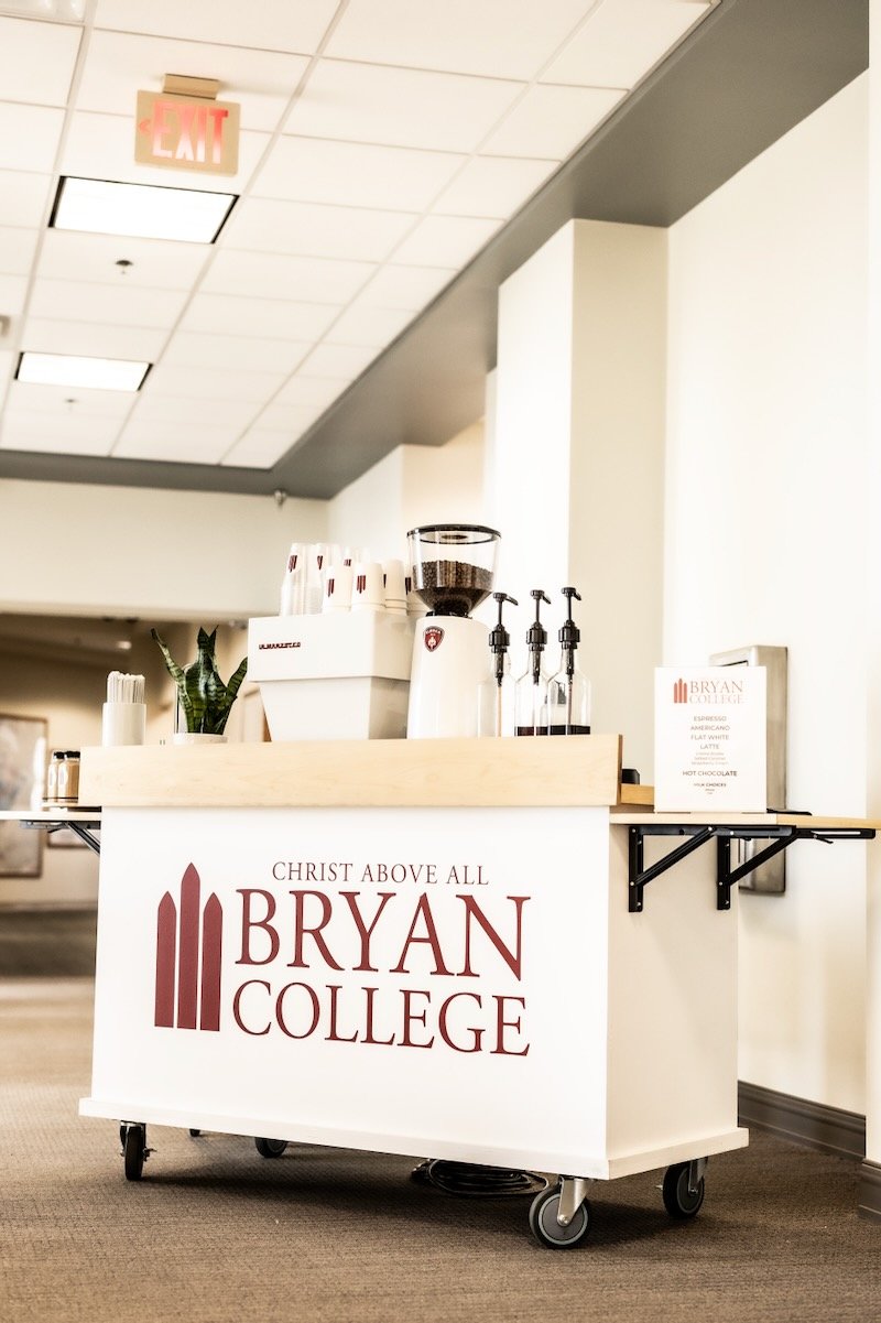 Bryan College branded coffee bar with cups, coffee beans, and espresso equipments in a school setting.