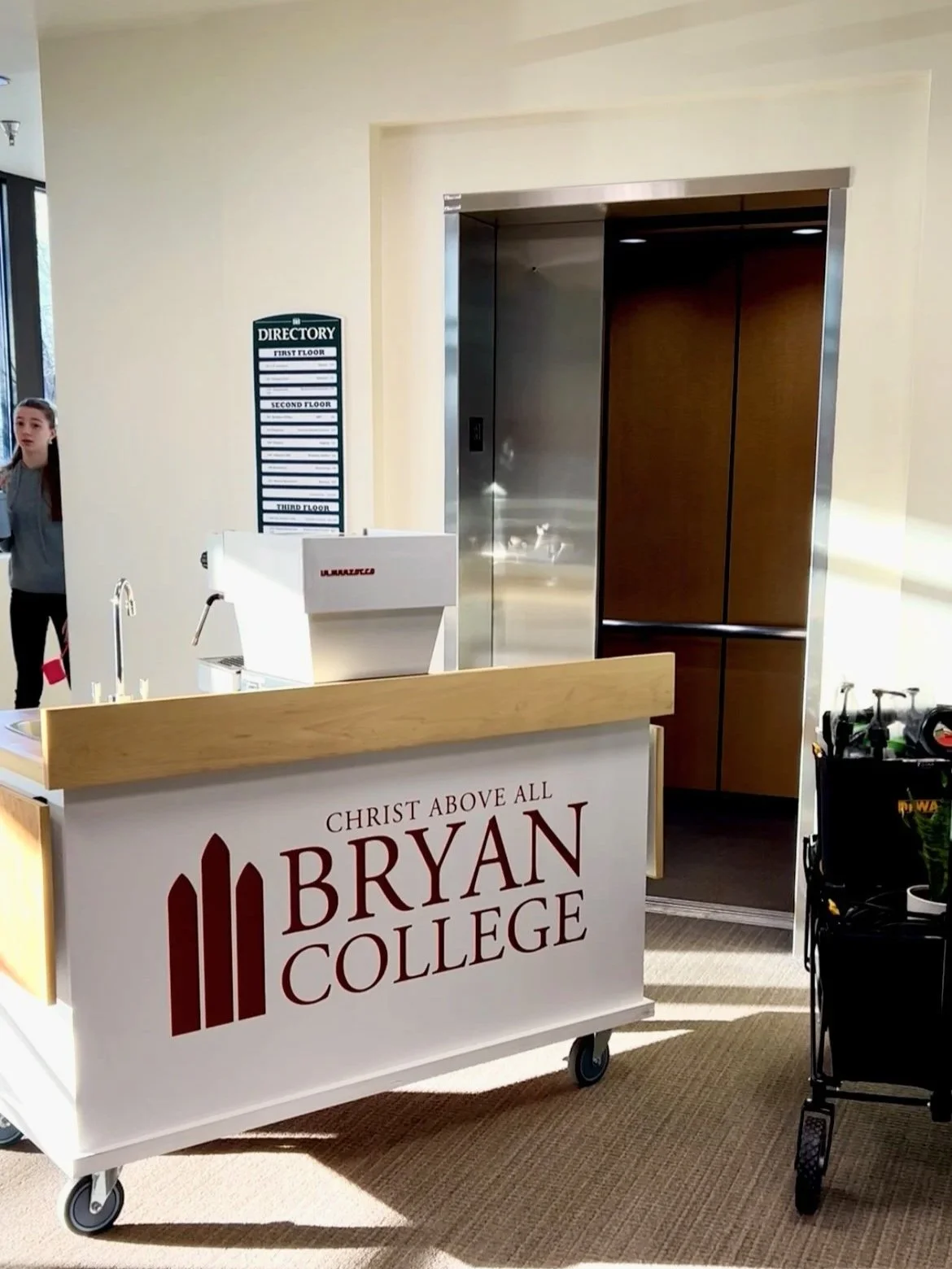 Bryan College reception desk with a sign saying 'Christ Above All Bryan College' and an elevator behind it.