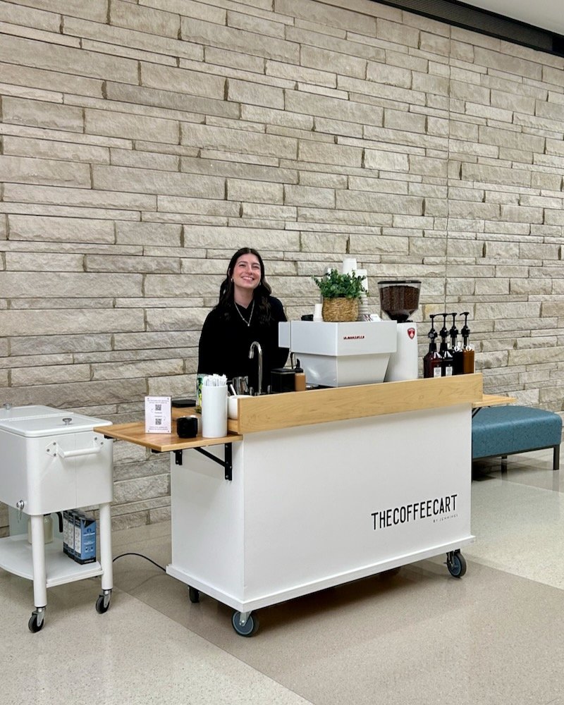 A smiling professional barista standing behind a mobile corporate event coffee bar with the logo 'THECOFFEE CART' at the College of Veterinary Medicine at the University of Tennessee Institute of Agriculture