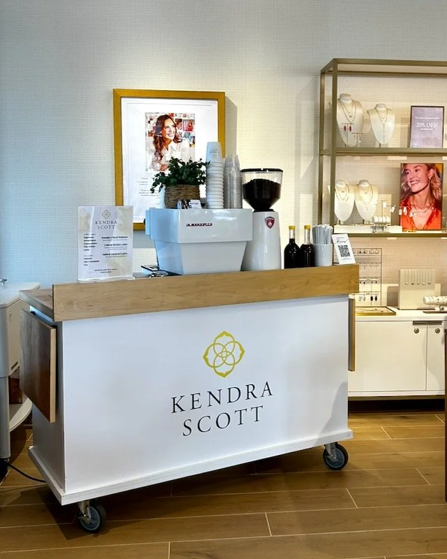 Kendra Scott jewelry store display with a reception counter, jewelry displays, and promotional posters.
