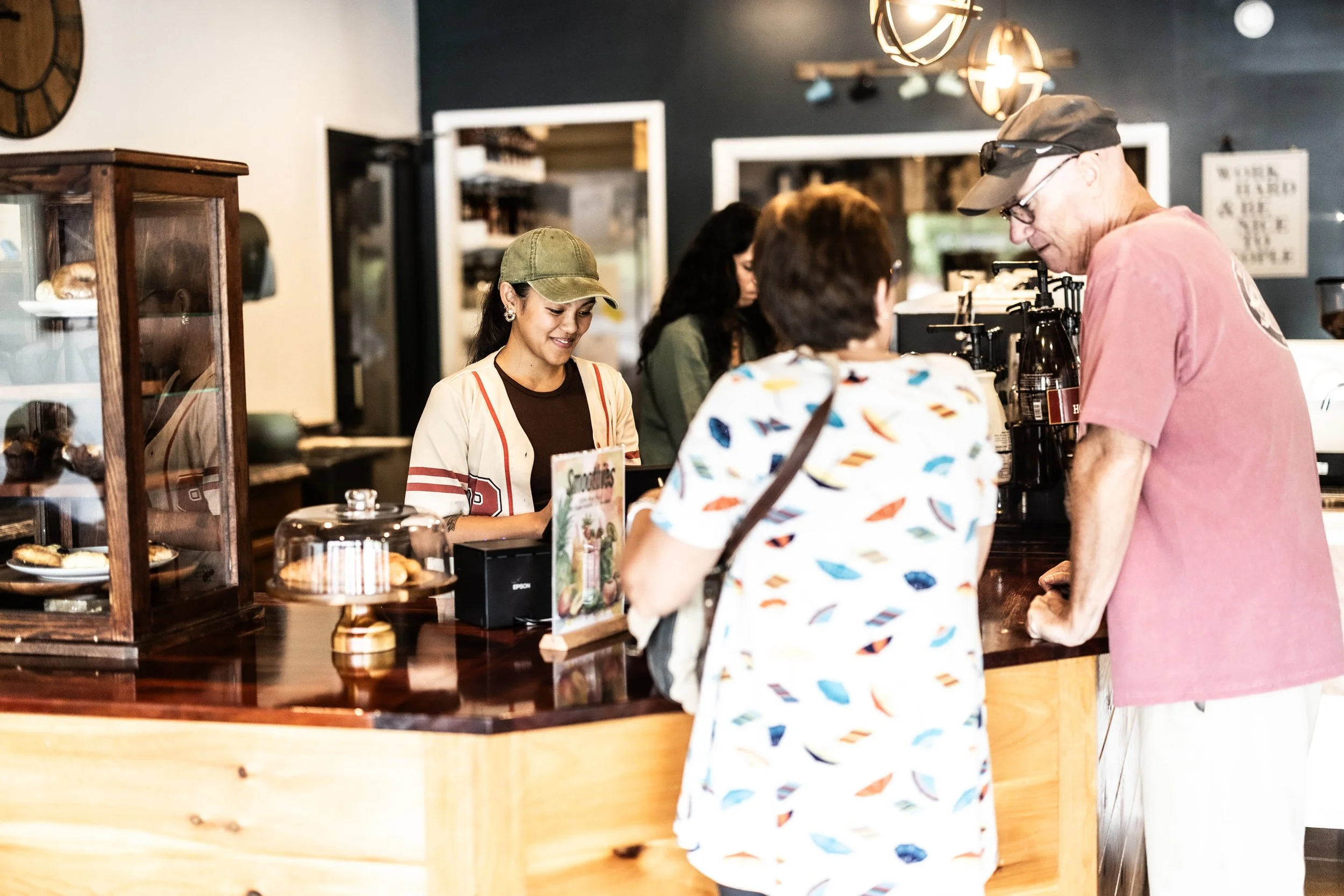 A group of customers at a coffee shop counter placing orders, with baristas preparing drinks behind the counter.
