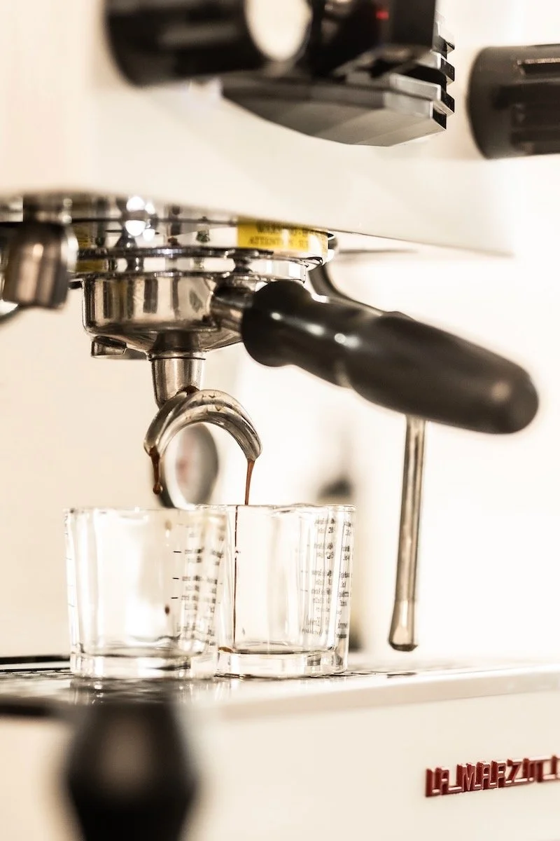 Close-up of a coffee espresso machine pouring hot coffee into two clear glass cups.