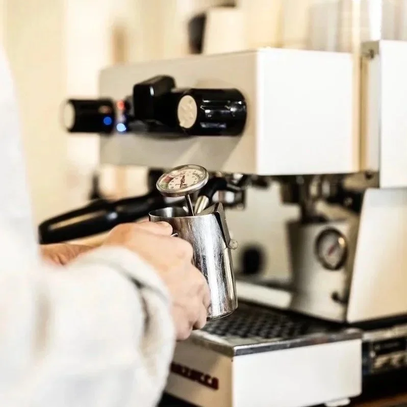 A barista tamping coffee grounds into a portafilter for an espresso machine.