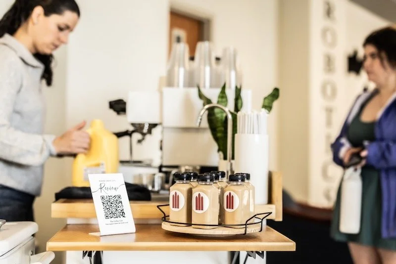 Table with custom branded bottle lattes and a menu card at a coffee shop, with two women in the background.
