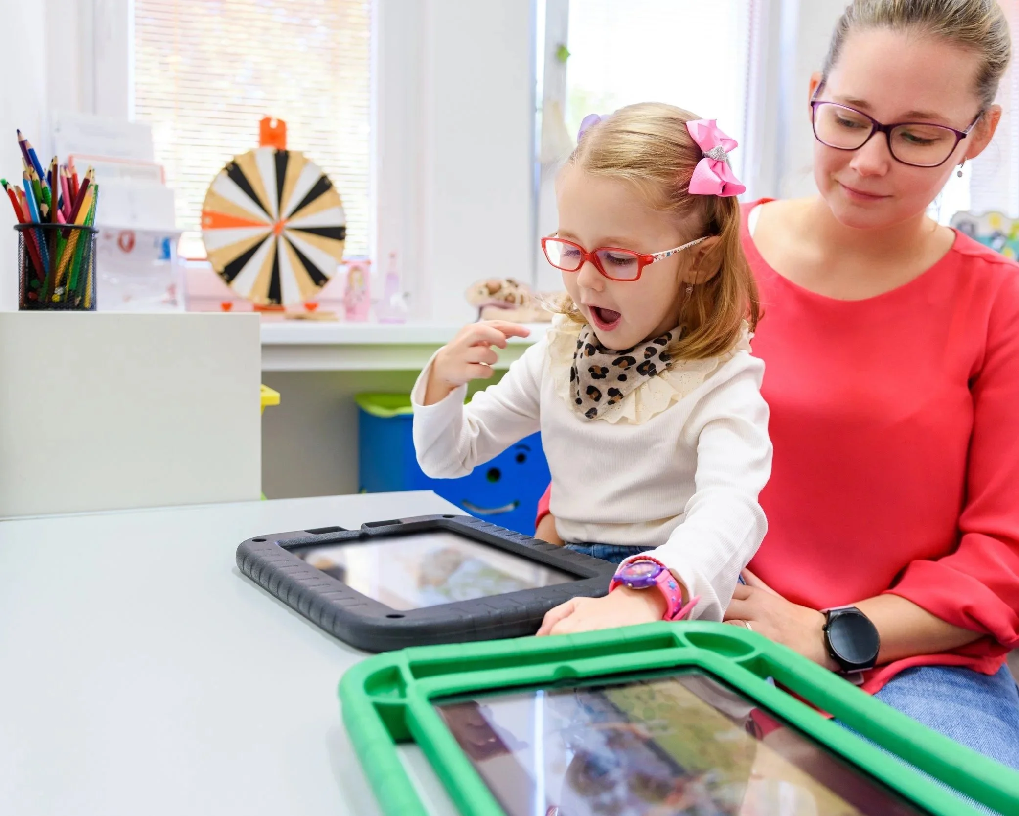 A young autistic girl sitting on her mom's lap at home during a speech therapy session focusing on AAC use and parent coaching to expand expressive language skills in Tustin, CA.
