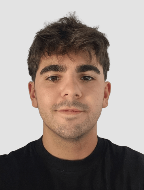 Primer plano de un joven con cabello castaño oscuro, cejas gruesas, piel clara y una expresión neutral, vestido con una camiseta negra, en un fondo gris claro.